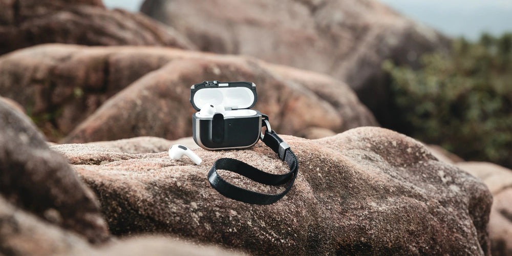 MAGEASY Odyssey outdoor AirPods Pro 3 case hanging by the strap beside a rock for adventure travel